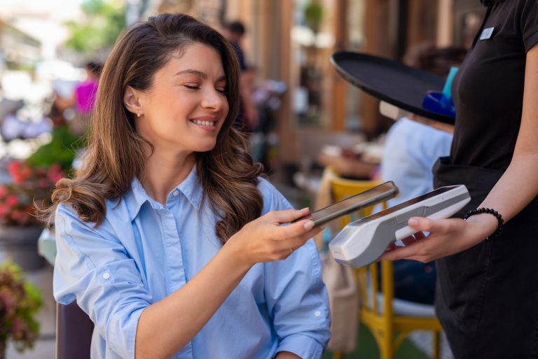 Woman making a cashless payment at a cafe using Pioneer Bank and NFC technology on her smartphone.